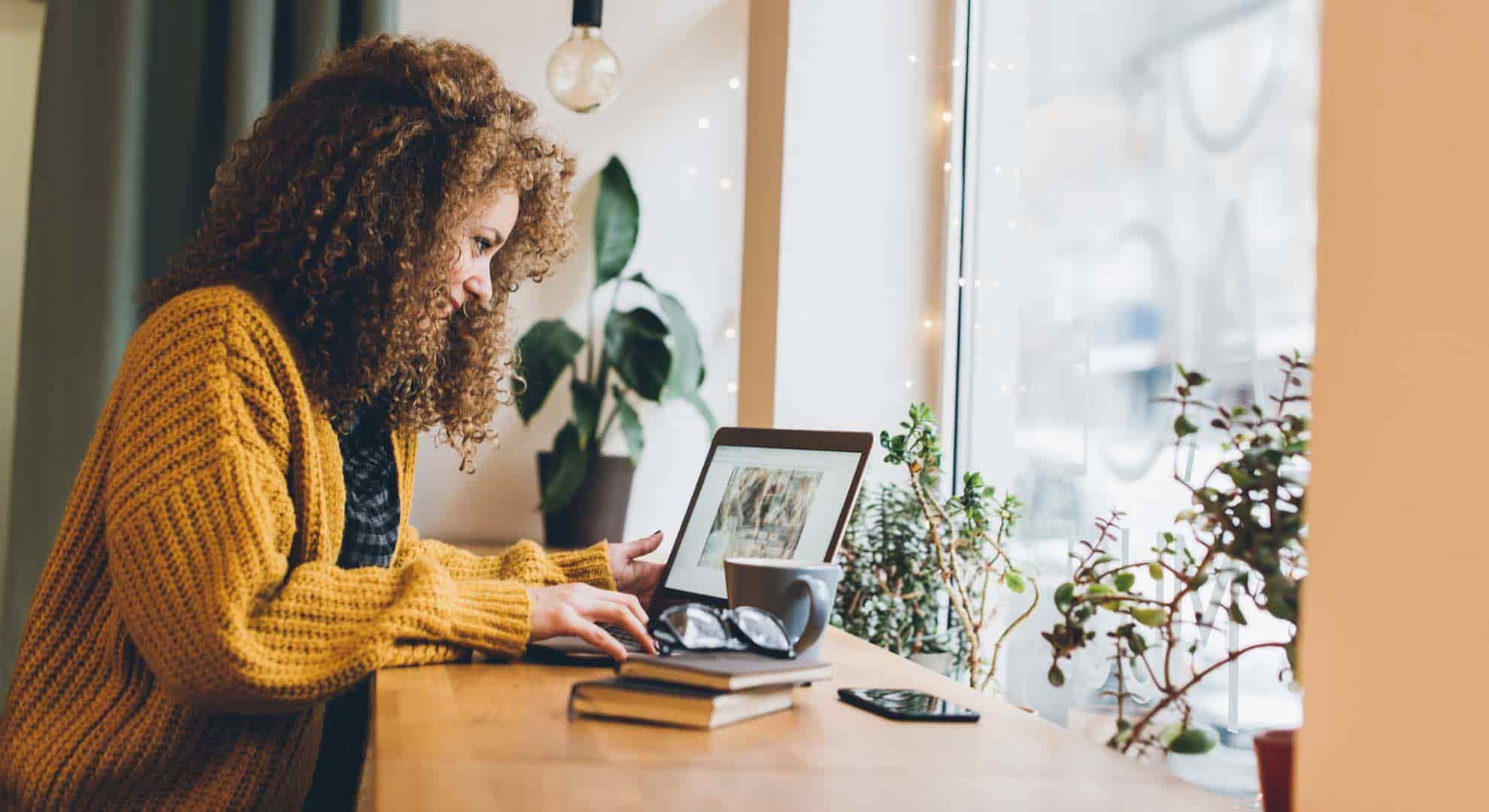 Photo of a woman sitting at a cafe window using her laptop