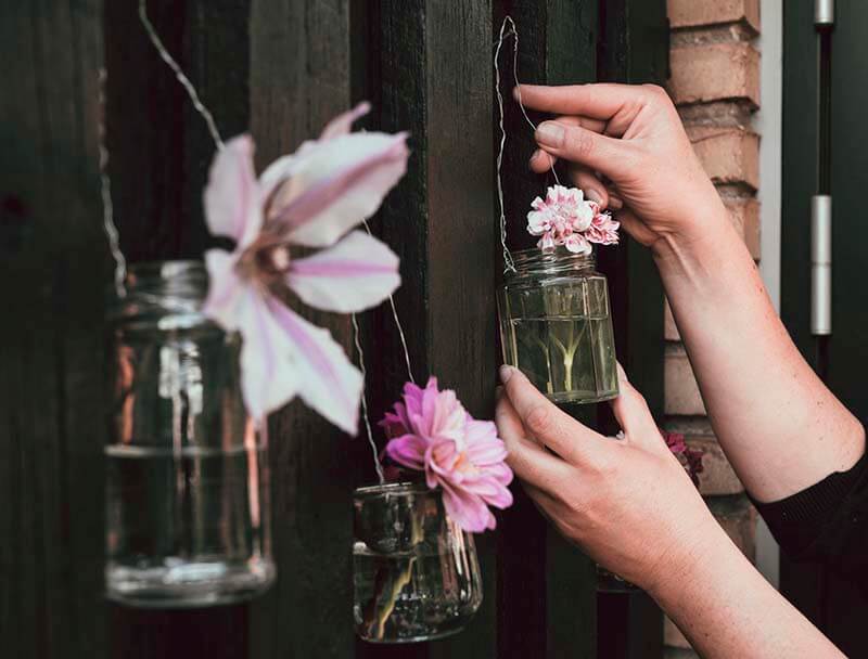 A person using a empty glass jar to hold flowers and hanging them from a fence