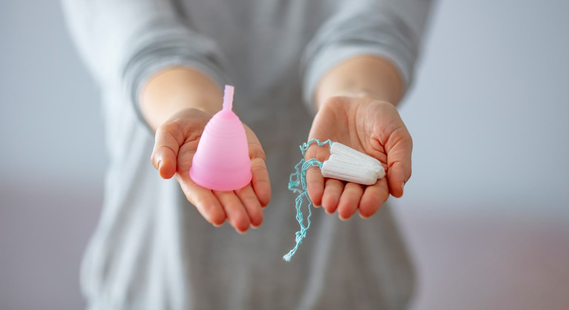 Woman holding tampons and menstrual cup in hands